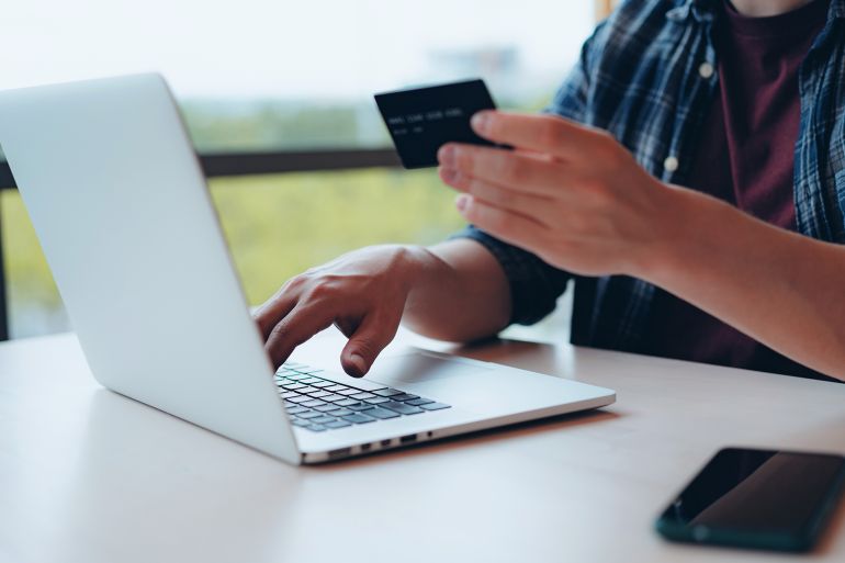 Young adult man entering credit card details to make online payment. Online shopping concept. Travel planning. Booking a holiday online.