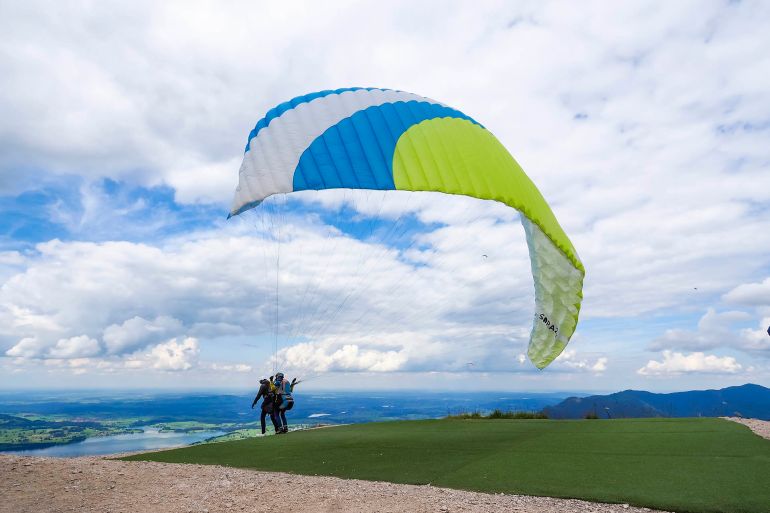 Fussen, Germany - 25 July 2020: A tandem paraglider is taking off from the launch pad on top of Mt Tegelberg (elev. 1881m) in the Ammergau Alps. Since the 1970s, Mt Tegelberg is a popular take-off point for hang gliders and paragliders.