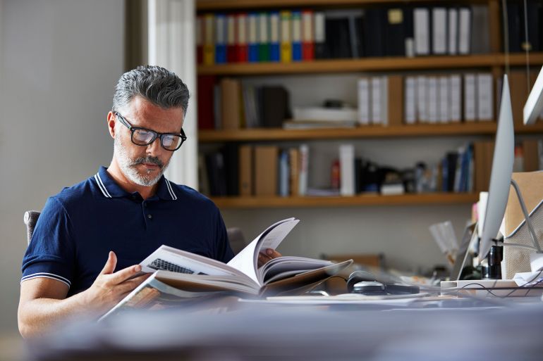 Mature businessman reading book at desk in office