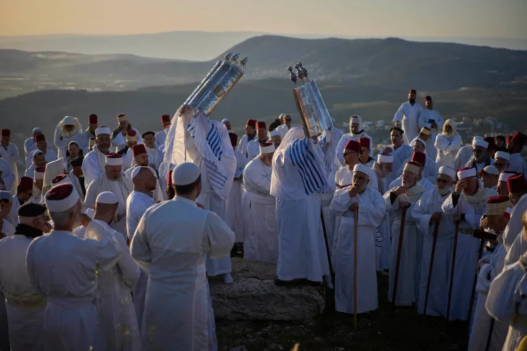 Members of the ancient Samaritan community, wrapped in a prayer shawls, hold up Torah scrolls as worshippers pray during the Passover pilgrimage at the religion's holiest site on the top Mt. Gerizim, near the West Bank town of Nablus, Friday, April 18, 2025. (AP Photo/Ohad Zwigenberg)